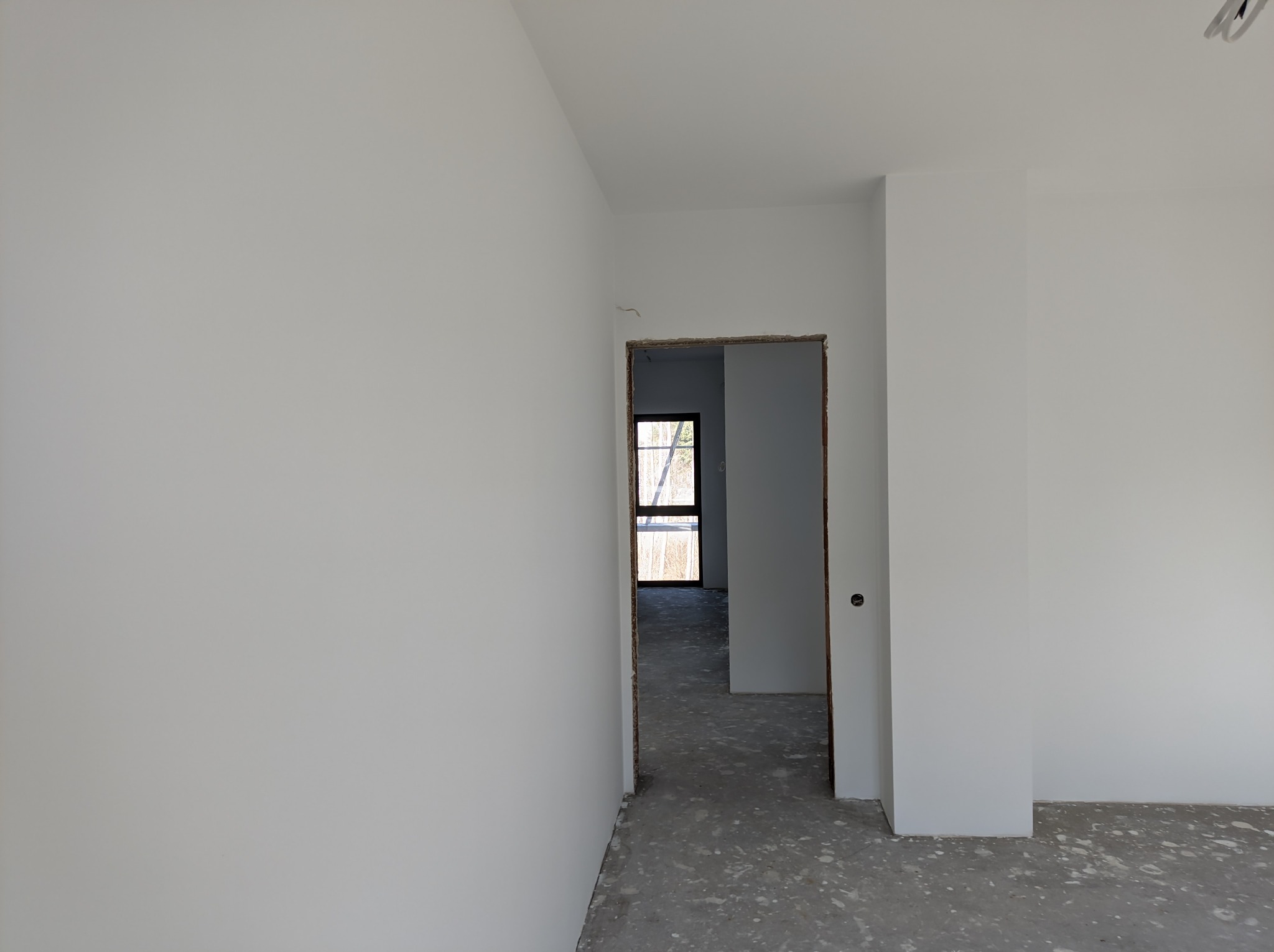 Wnętrze po świeżym malowaniu na biało, widoczne ślady farby na szarym betonie, surowe ościeżnice drzwiowe i okno w tle.