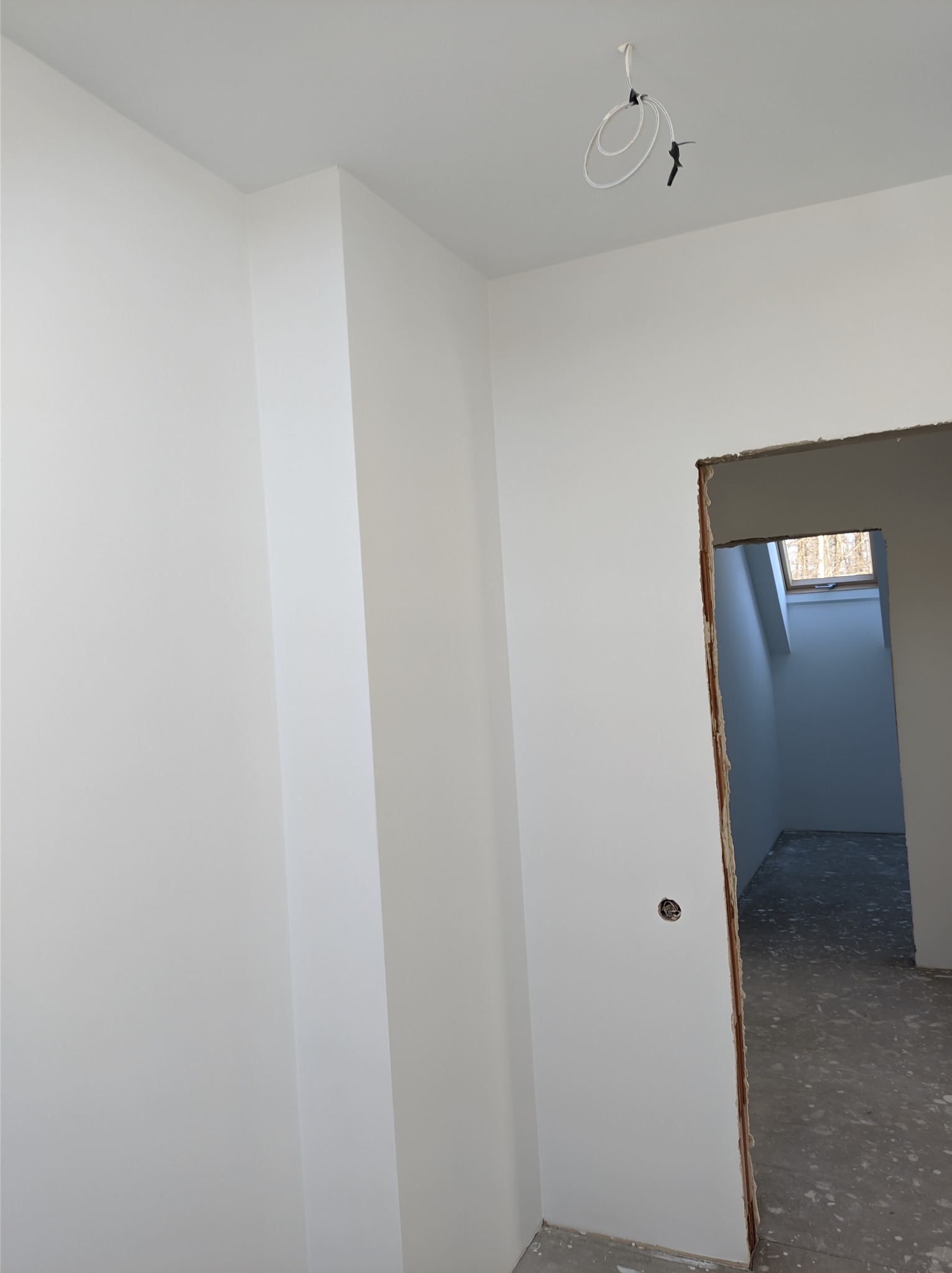 Świeżo pomalowane na biało wnętrze z widocznym otworem drzwiowym i wystającymi przewodami z sufitu.