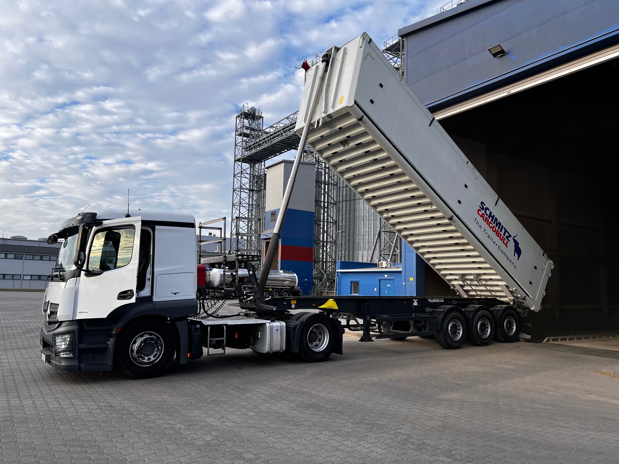 Ciężarówka Mercedes-Benz z naczepą wywrotką Schmitz Cargobull pod kątem, gotowa do rozładunku w magazynie zbożowym
