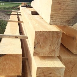 Tartak Andrzej Niesterczuk - Świeżo przetarte, jasne belki z widocznymi słojami drewna, ułożone w stos w Mieleszki-Kolonia, z polami i lasem w tle.