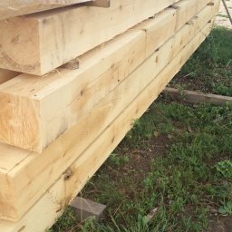 Tartak Andrzej Niesterczuk - Stos świeżo obrobionych, jasnych belek drewnianych ułożonych na trawie.