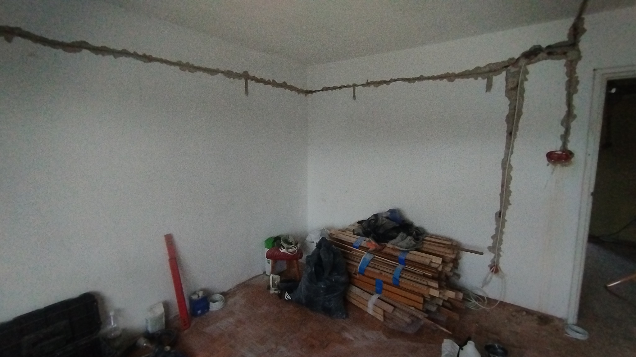 Przygotowanie bruzd w ścianach pod instalację elektryczną, widoczne przewody i puszki elektryczne, w tle zgromadzone materiały i narzędzia.