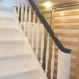 RDK. Serwis - Białe schody z czarną poręczą, widok z dołu, po malowaniu, w tle pralka i drewniany stelaż łóżka.