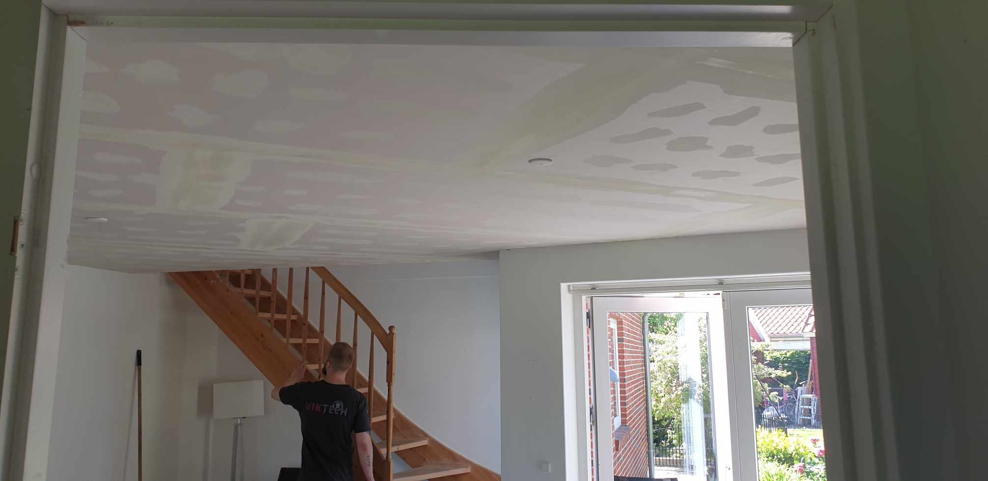 Przygotowanie sufitu do malowania: widoczne ślady po szpachlowaniu w pomieszczeniu z drewnianymi schodami i białymi drzwiami balkonowymi.