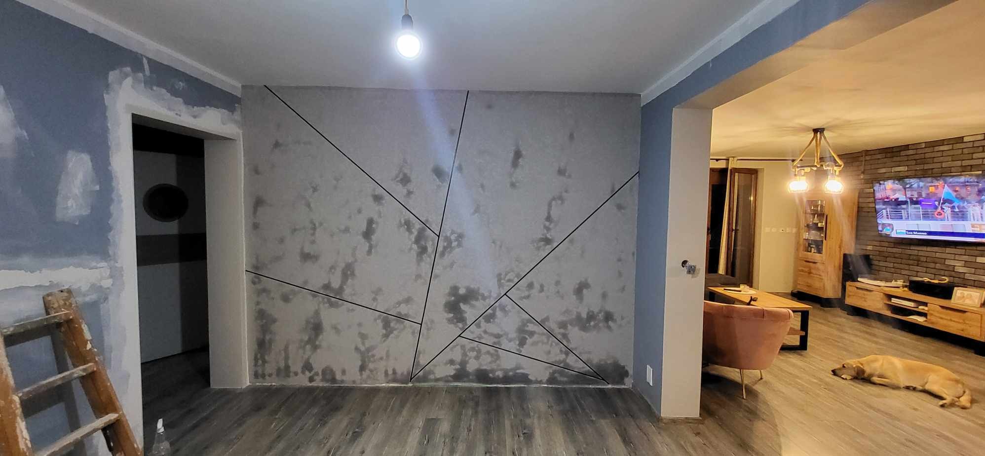 Pokój po odświeżeniu ścian z dekoracyjną strukturą i geometrycznymi liniami, widoczny fragment drabiny malarskiej i otwarte przejście do salonu z ceglaną ścianą i psem leżącym na podłodze.