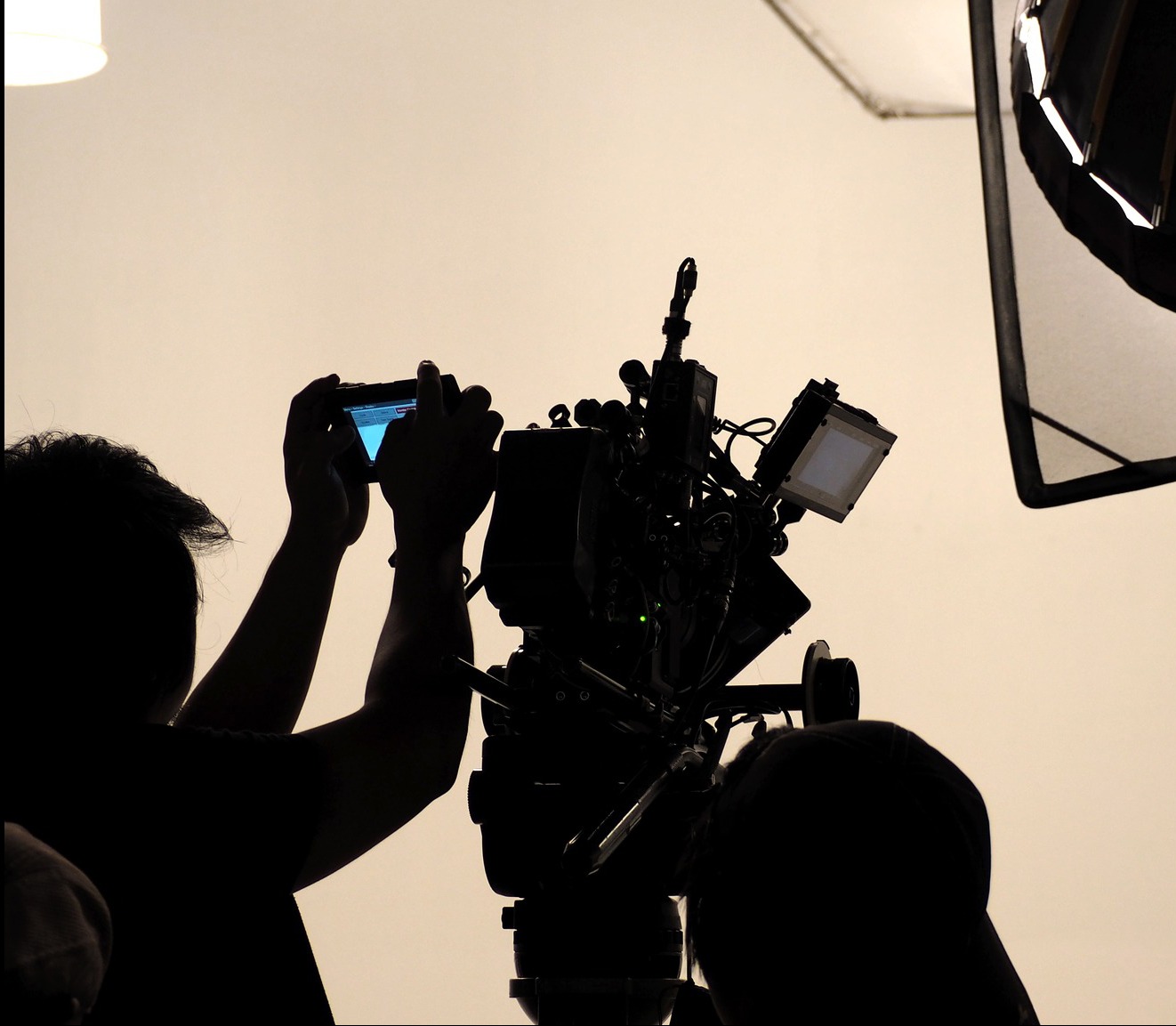 Ekipa filmowa w trakcie pracy, widoczna kamera filmowa z monitorem, softbox oświetleniowy i osoba trzymająca smartfon, wszystko w silnym kontraście.