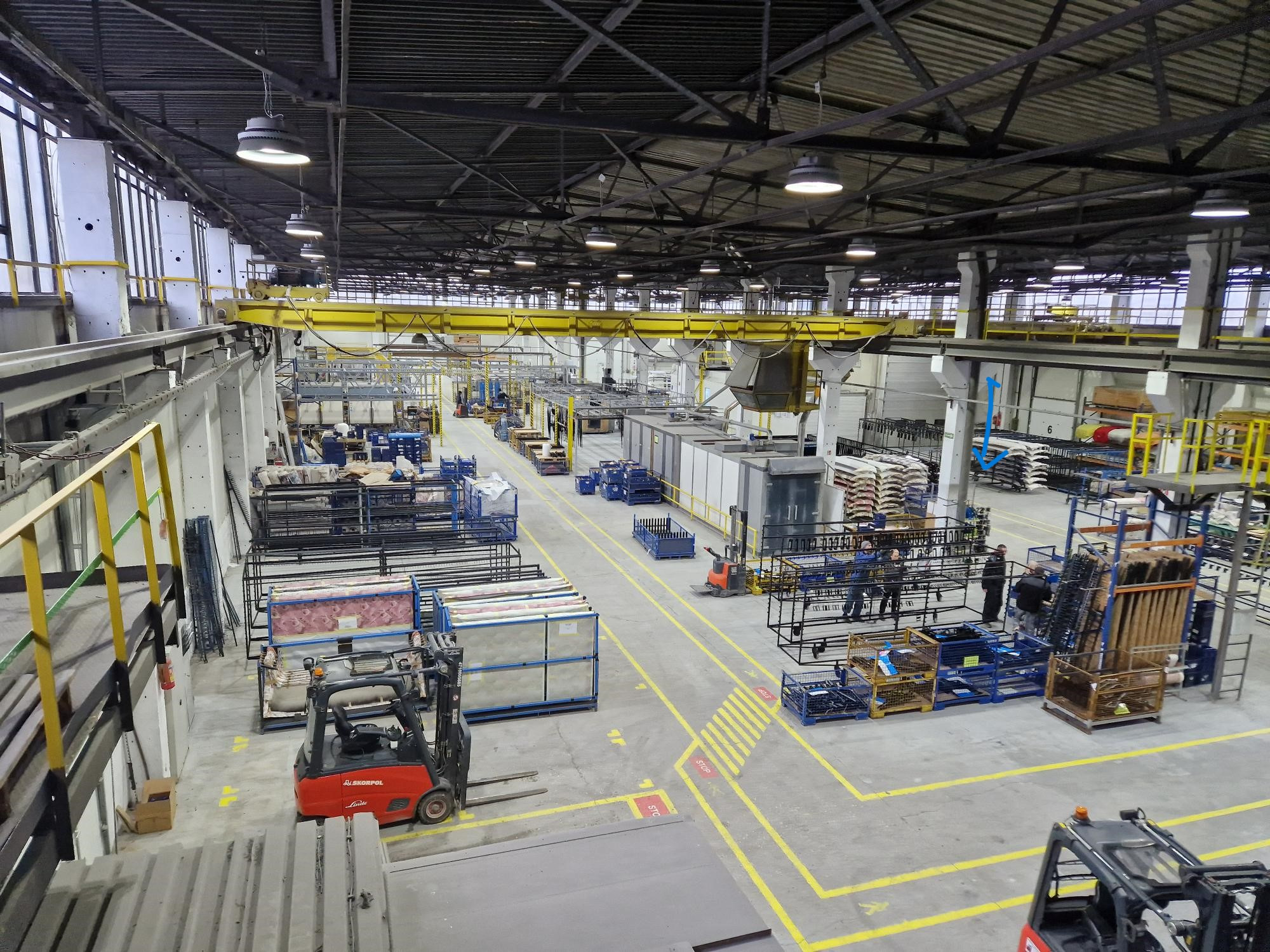 Szeroki kadr hali produkcyjnej w Wąchocku, z widocznymi wózkami widłowymi, różnymi elementami metalowymi przygotowanymi do obróbki oraz suwnicą pod stropem.