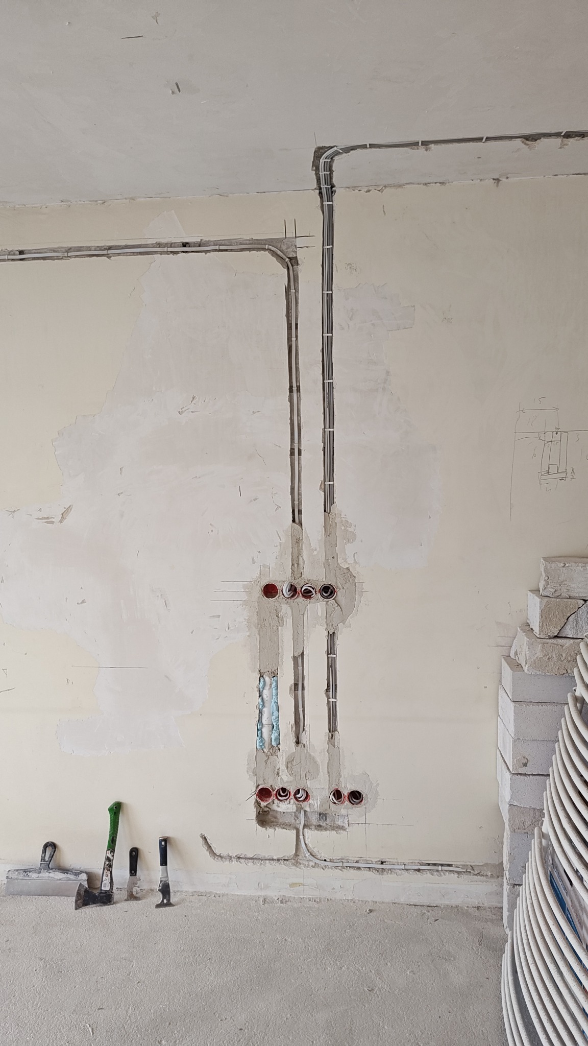 Ściana w trakcie instalacji elektrycznej: widoczne kable w bruzdach, puszki elektryczne, pianka montażowa, narzędzia (szpachelki, młotek) oraz bloczki z betonu komórkowego.