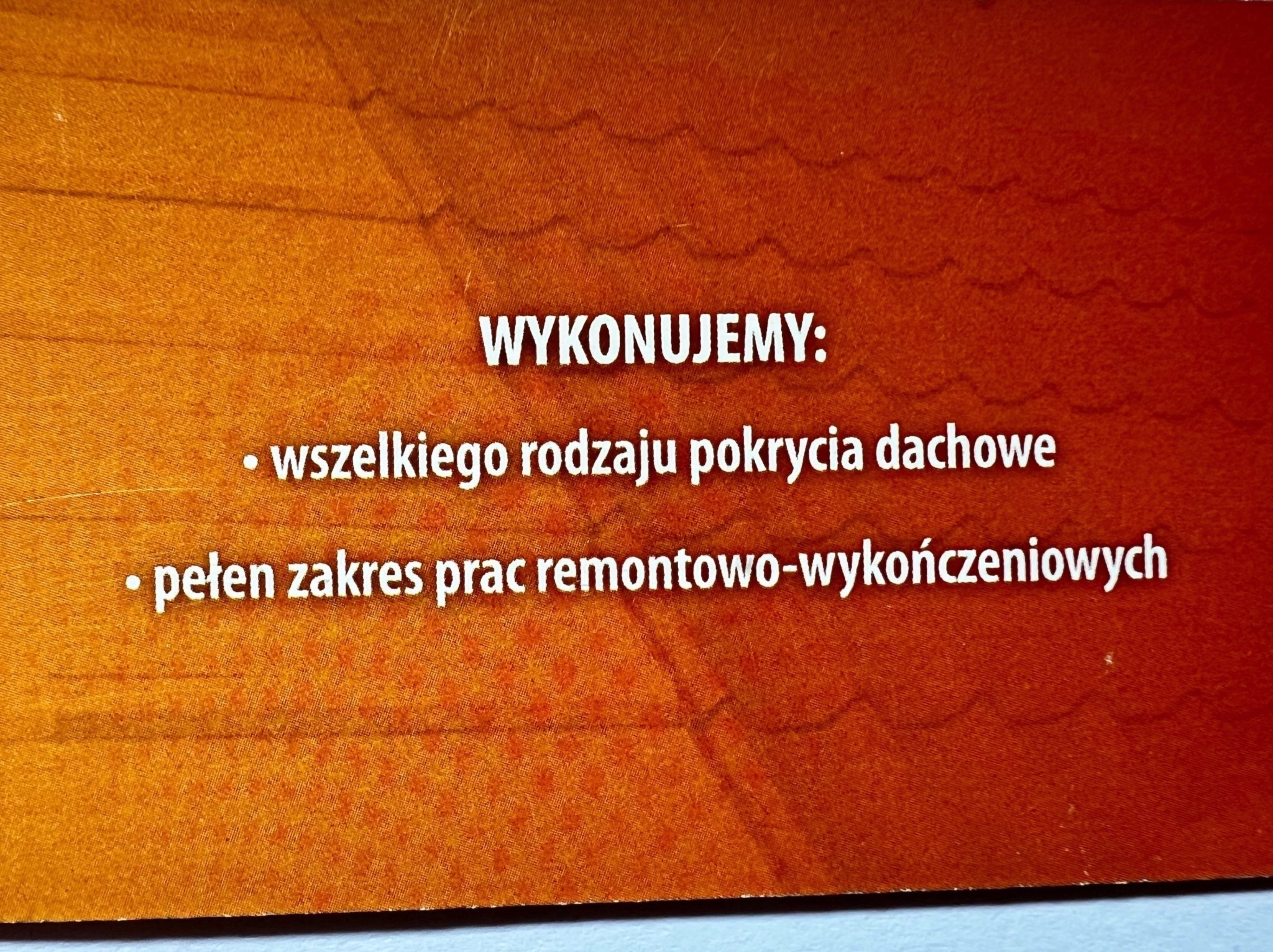 Tekst na pomarańczowo-czerwonym tle informujący o wykonywaniu pokryć dachowych i prac remontowo-wykończeniowych.