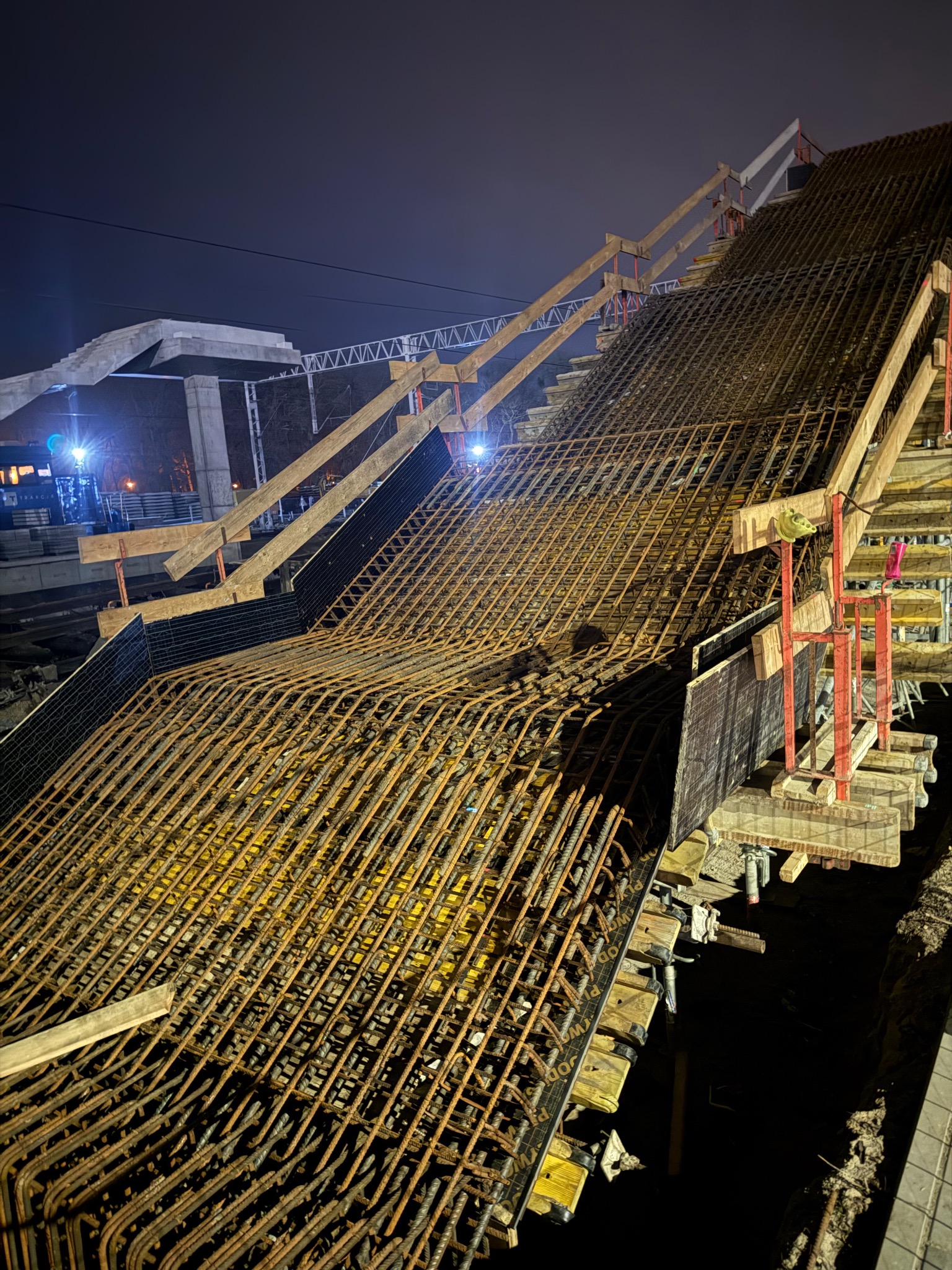 Konstrukcja zbrojeniowa pod budowę schodów żelbetowych w Szczecinie, widoczna siatka z prętów stalowych i drewniane szalunki w nocnym oświetleniu.