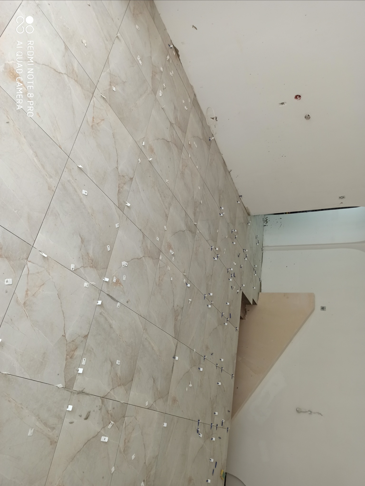 Ściana w trakcie układania płytek imitujących marmur, widoczne krzyżyki dystansowe, surowy stan wykończenia.