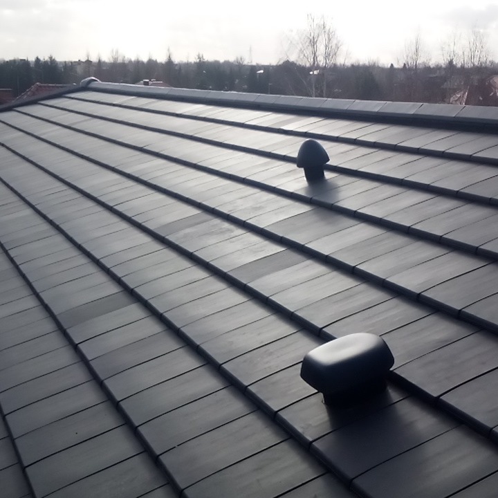 Nowy, grafitowy dach z dachówki ceramicznej z dwoma kominkami wentylacyjnymi, widok z góry na tle drzew i zabudowań.