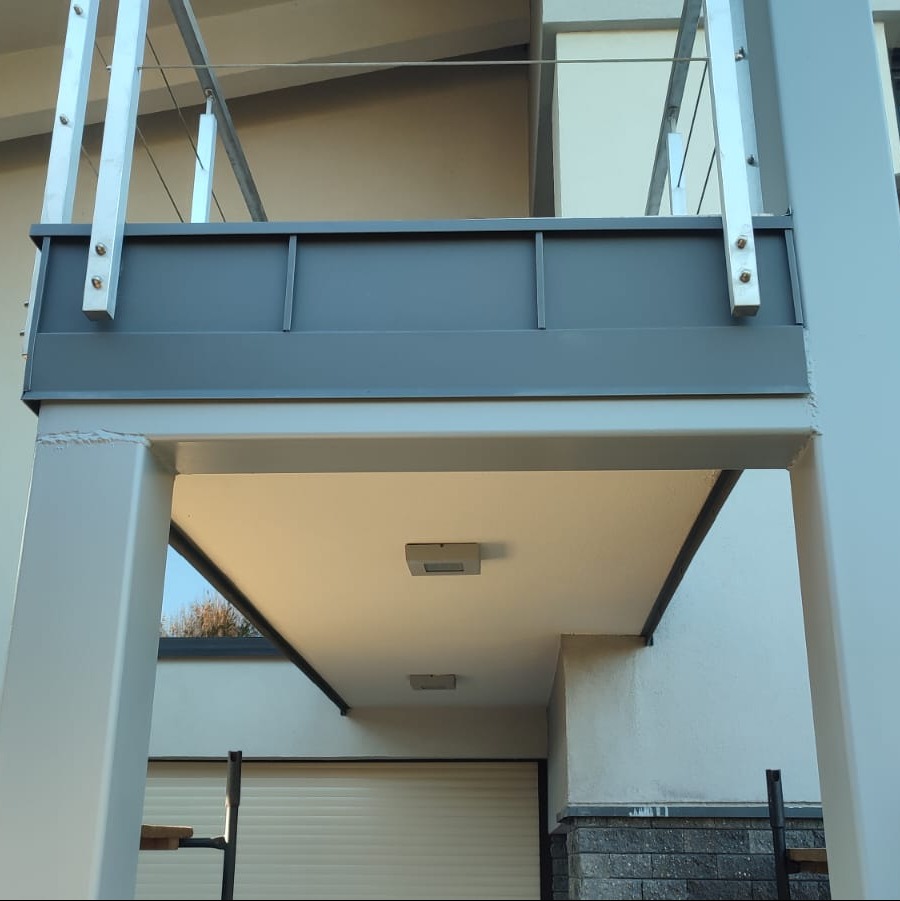 Metalowa obróbka blacharska balkonu nad wjazdem do garażu z roletą, widok z dołu.