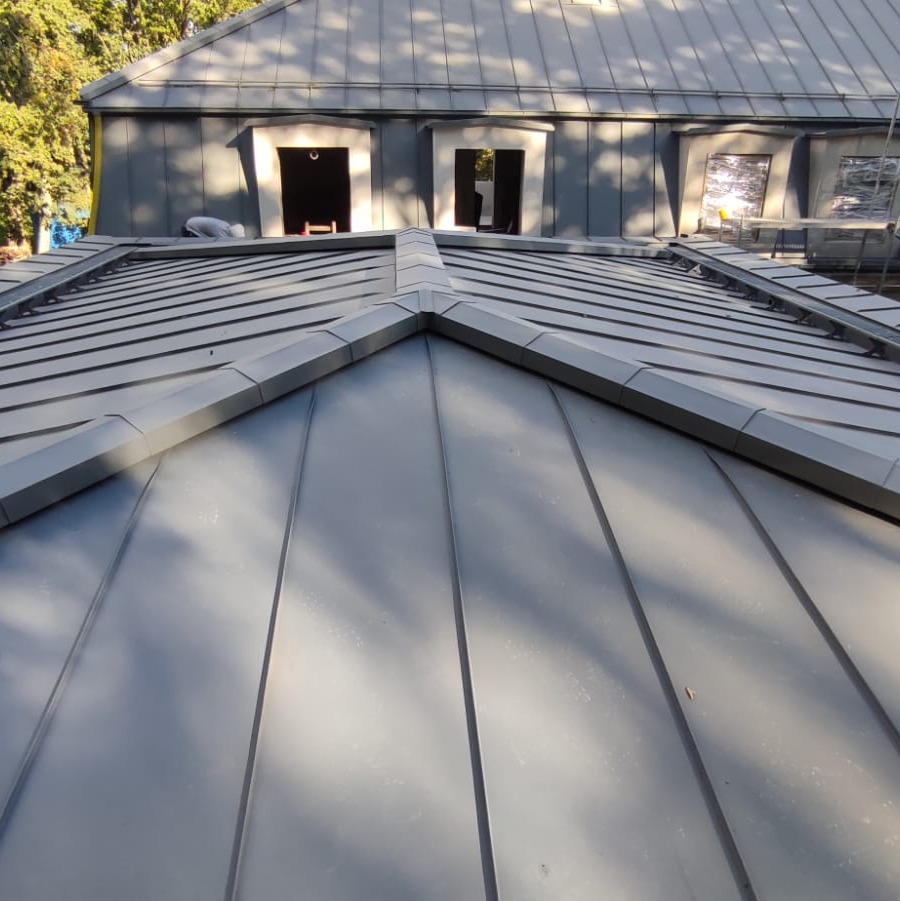 Szary dach z blachy trapezowej, widoczne okna dachowe w trakcie montażu oraz fragment dachu sąsiedniego budynku