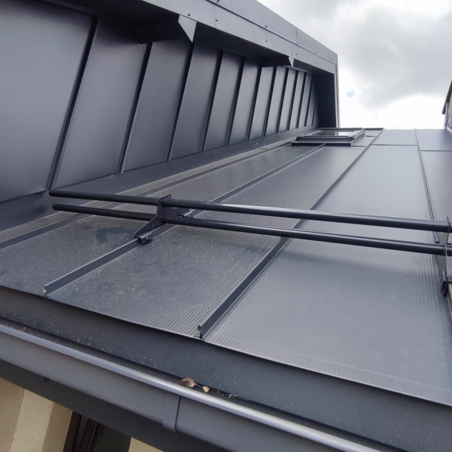 Nowoczesny, grafitowy dach panelowy z systemem odśnieżania, widok z dołu na tle pochmurnego nieba.