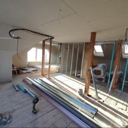 WRO IVESTALL - Poddasze w trakcie adaptacji: widoczne profile metalowe, płyty karton-gips na ścianach, drewniane słupy wzmacniające konstrukcję, instalacje elektryczne pod sufitem oraz narzędzia do cięcia profili...