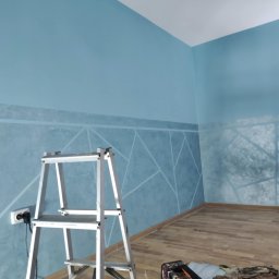 WRO IVESTALL - Niebieska ściana z geometrycznym wzorem, wykonana techniką dekoracyjną, widoczna aluminiowa drabina i fragment podłogi z paneli.