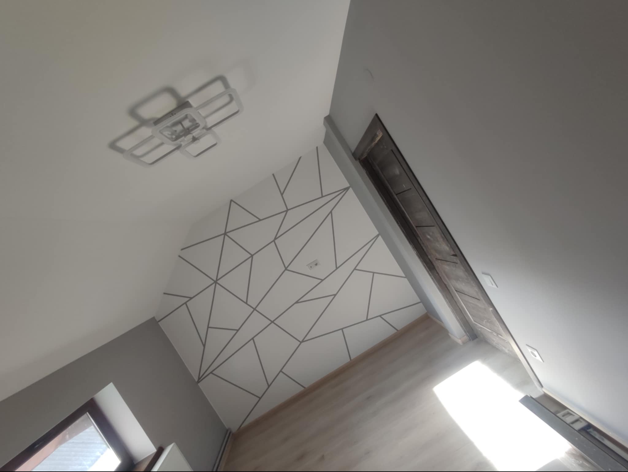 Biała ściana z geometrycznym wzorem z szarych linii, nowoczesna lampa sufitowa, widok z dołu, jasne wnętrze po remoncie.
