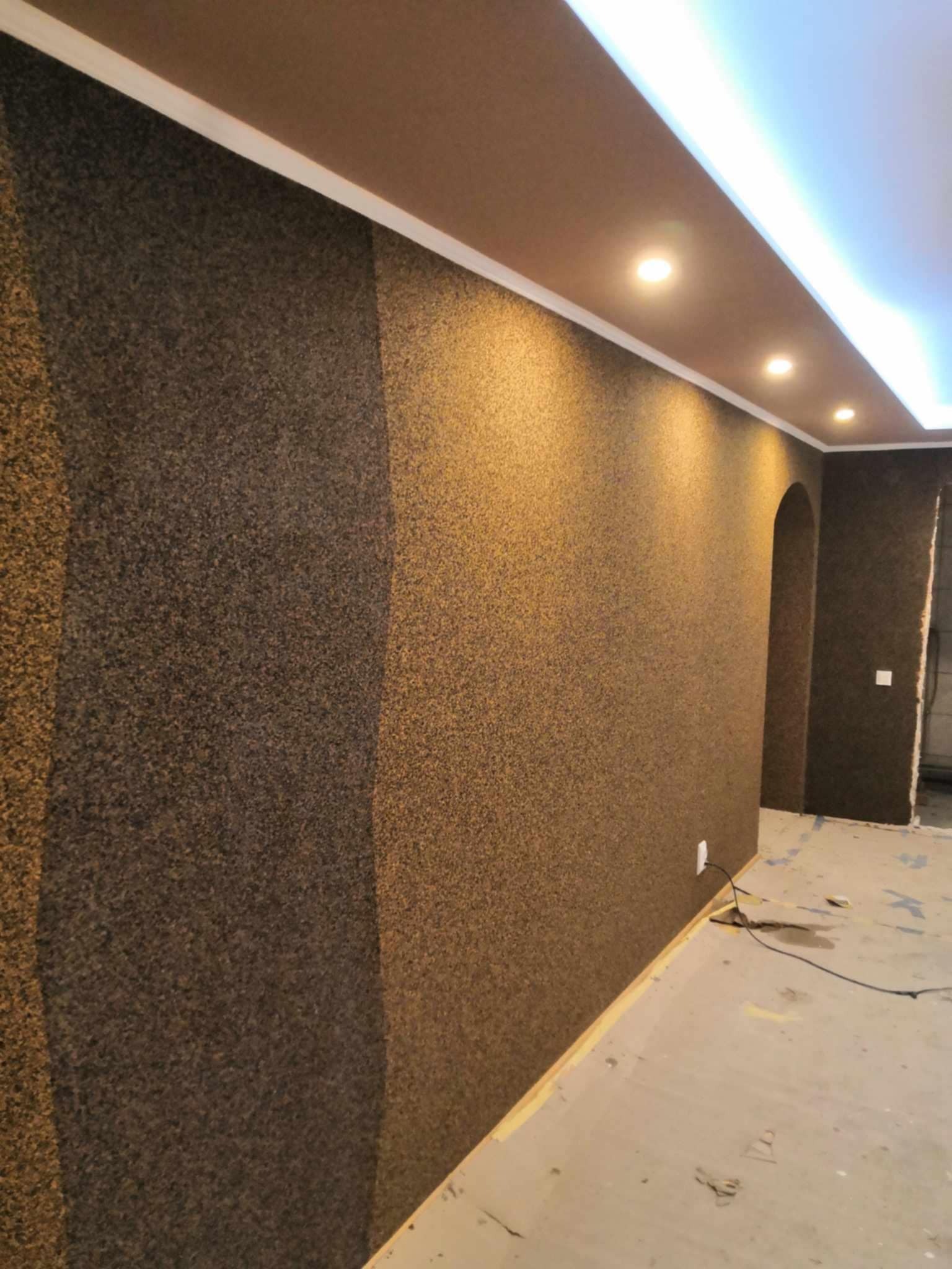Teksturowana ściana w odcieniach brązu i złota z dekoracyjnym podziałem na panele, oświetlona punktowo i listwą LED, widoczny fragment sufitu i podłogi w trakcie prac wykończeniowych.