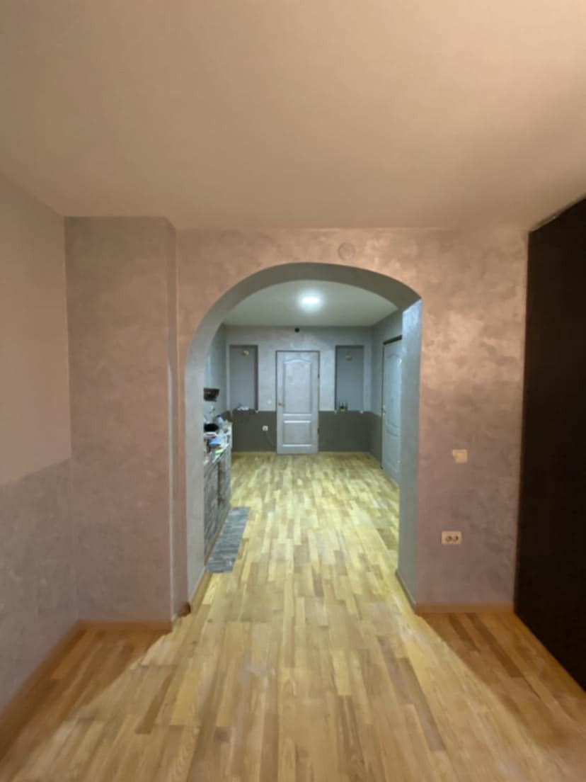 Wnętrze mieszkania po remoncie: parkiet ułożony w jodełkę, ściany pomalowane na szaro z efektem dekoracyjnym, przejście w kształcie łuku do kolejnego pomieszczenia.