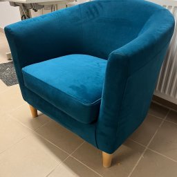 YH Tapicer - Turkusowy fotel klubowy z drewnianymi nóżkami, stojący na kafelkach, z widoczną maszyną do szycia w tle.