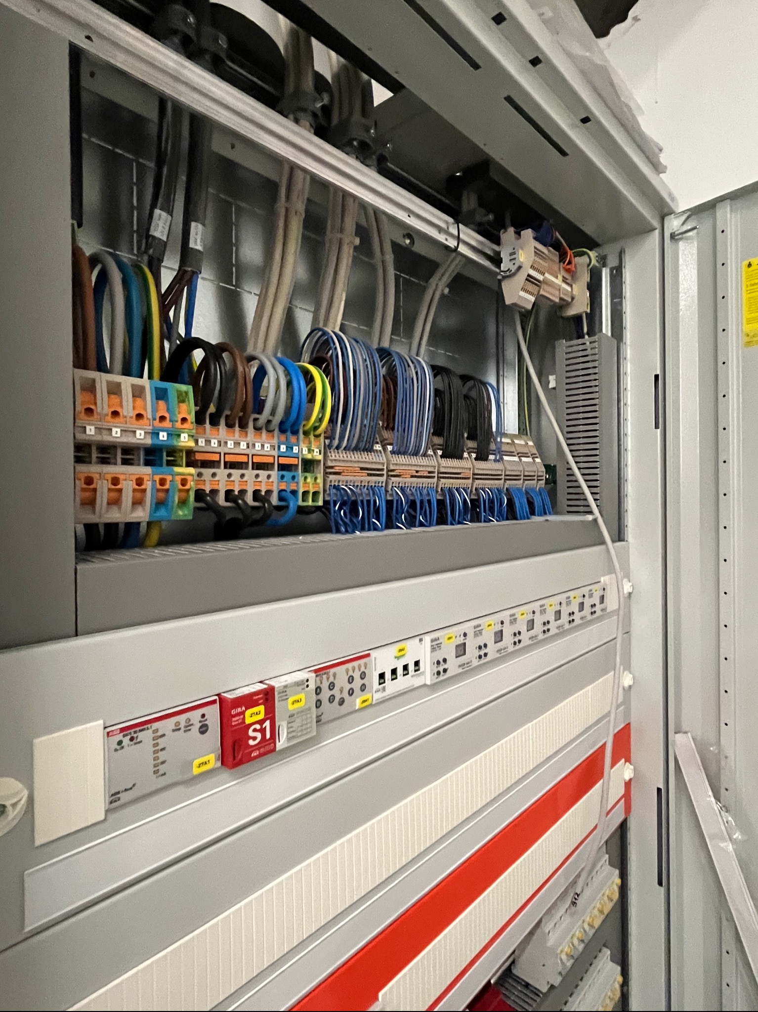 Szczegółowe ujęcie wnętrza szafy sterowniczej z przewodami w różnych kolorach, listwami zaciskowymi i modułami elektronicznymi. Widoczne elementy instalacji elektrycznej.