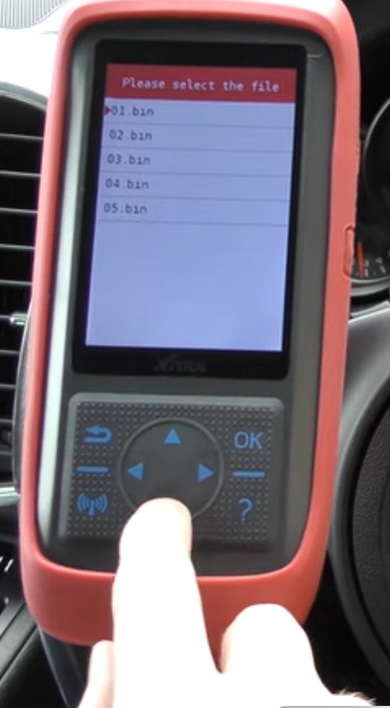 Diagnostyczny skaner samochodowy XTOOL z czerwonym obramowaniem, wyświetlający listę plików .bin, obsługiwany palcem w trakcie przeglądu pojazdu.