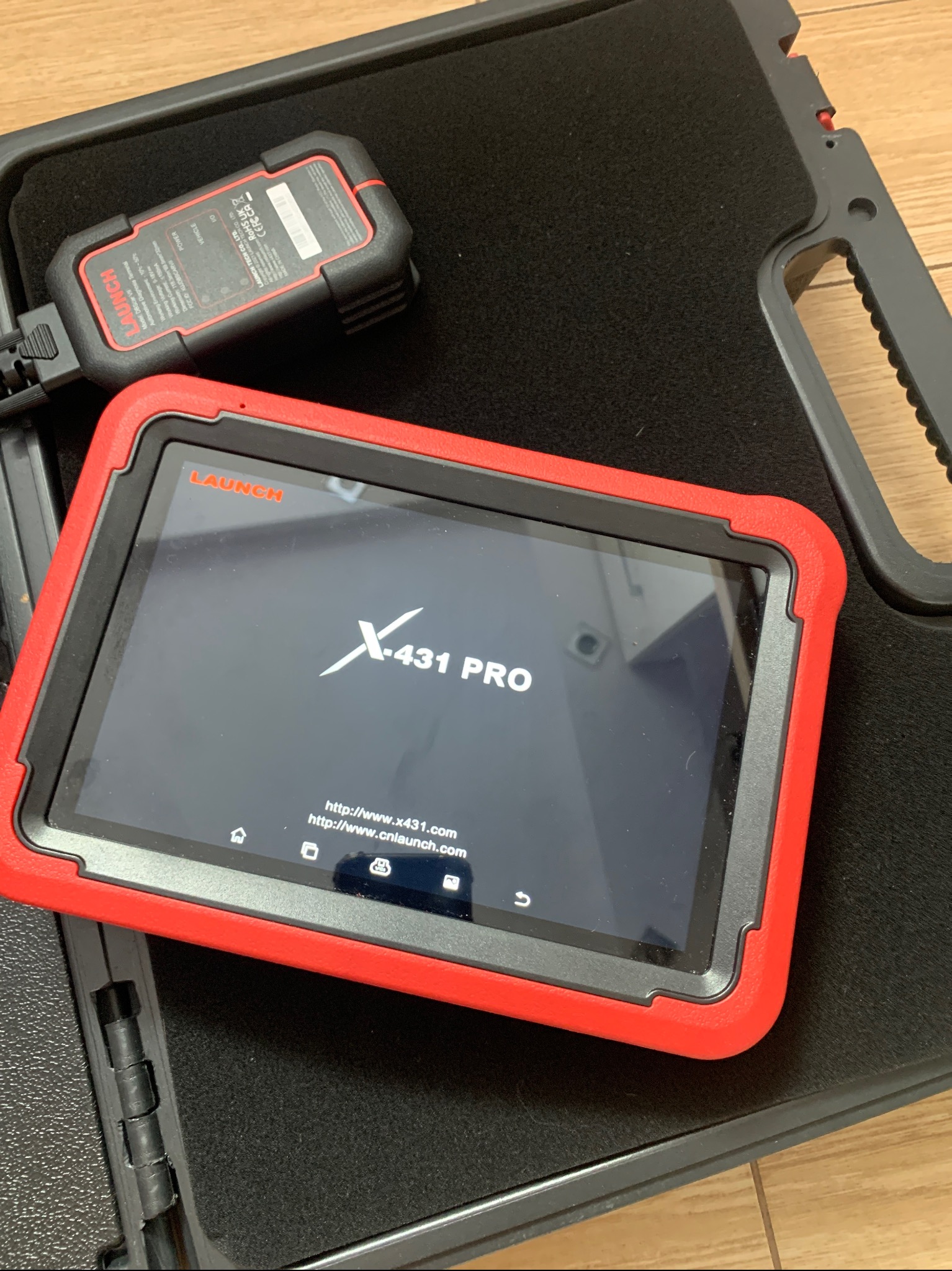 Tablet diagnostyczny Launch X-431 PRO z podłączonym adapterem, leżący w czarnym futerale z gąbką, używany do diagnostyki samochodowej.