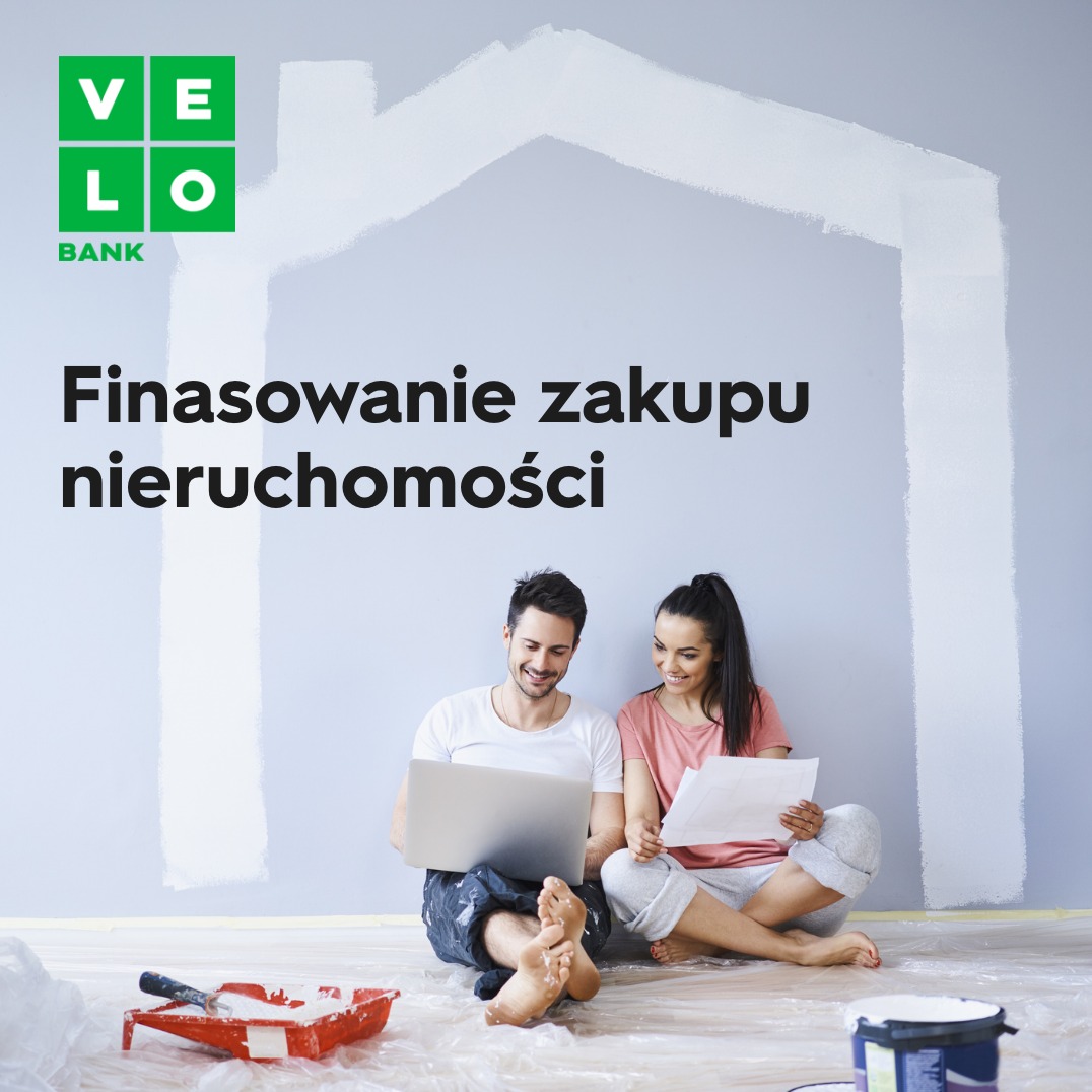 Para siedzi na podłodze z laptopem i dokumentami, za nimi ściana z namalowanym konturem domu, obok akcesoria malarskie, logo VeloBank u góry po lewej.
