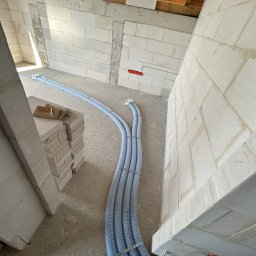 HYDRO-TECH RAFAŁ JAWORSKI - Wnętrze w trakcie instalacji rekuperacji: widoczne niebieskie rury wentylacyjne prowadzone wzdłuż surowych ścian z betonu komórkowego, z widocznymi elementami drewnianej konstrukcji dachu.