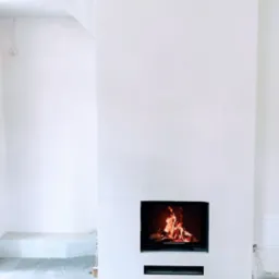 Nowoczesny, minimalistyczny kominek z czarną obudową i paleniskiem w jasnym, surowym wnętrzu. Widoczne detale wykończeniowe i kratki wentylacyjne.