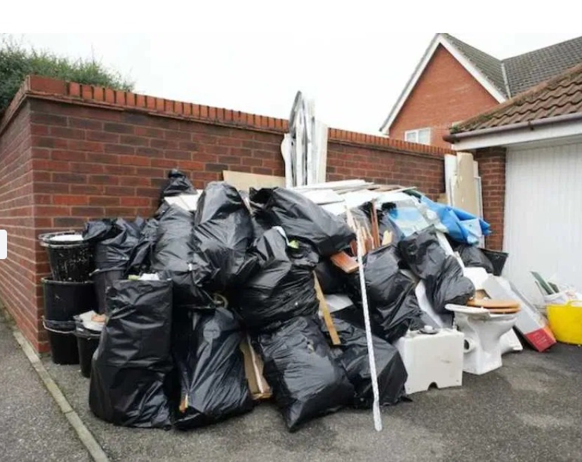 Sterta czarnych worków na śmieci, gruzu i starej toalety przed ceglanym budynkiem i garażem.