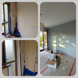 MS Michał Sikorski - Pokój w trakcie remontu: ściana z usuniętą starą farbą i resztkami niebieskiej taśmy malarskiej, zabezpieczone okno folią, oraz fragment ściany po świeżym pomalowaniu na szaro, z widocznym odbiciem...