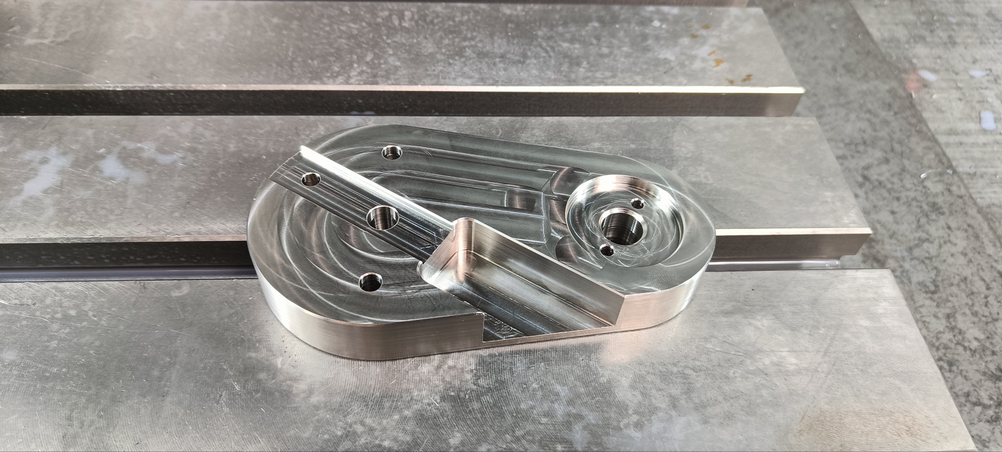 Precyzyjnie wykonany, metalowy element z licznymi otworami, obrobiony w Świdniku, leży na metalowej powierzchni roboczej. Widoczne ślady po obróbce.