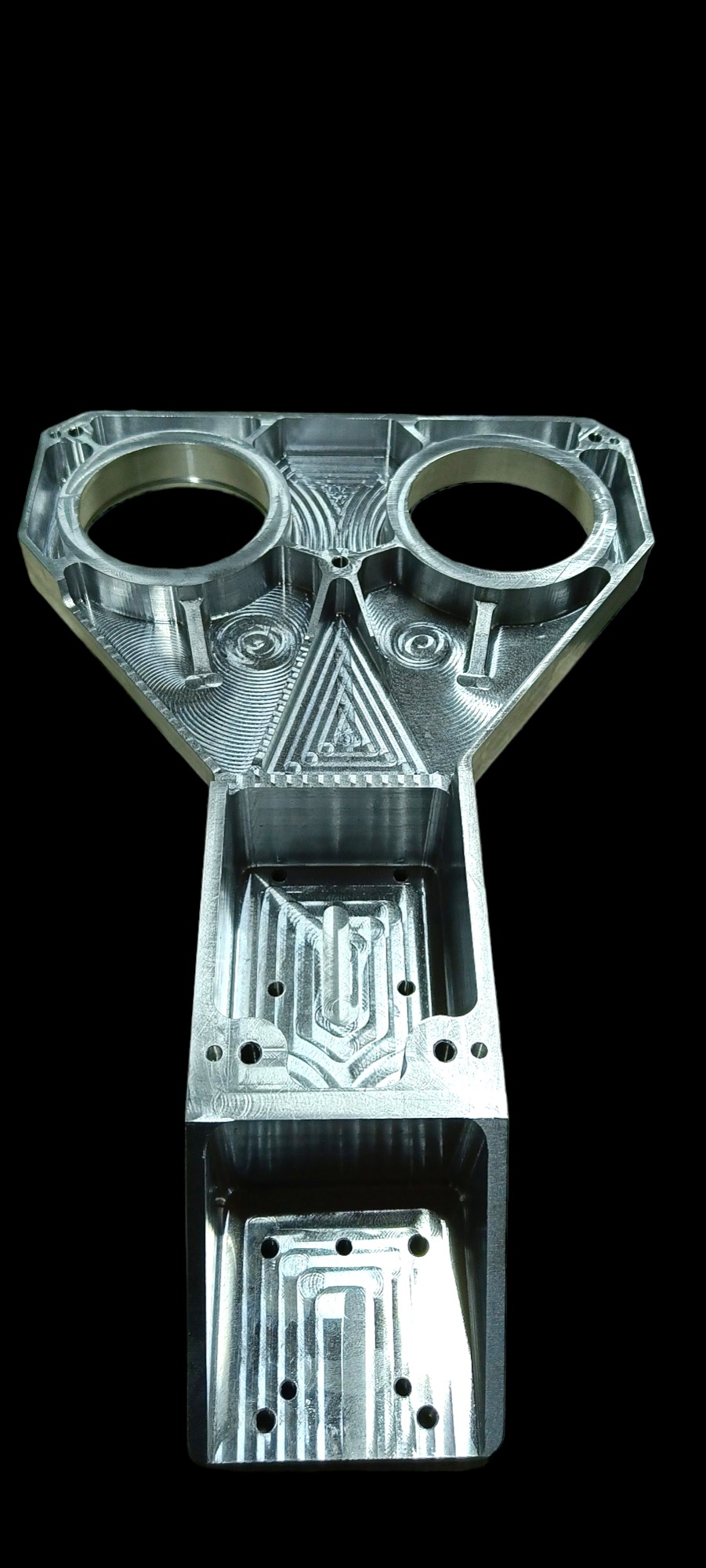 Precyzyjnie obrobiony, srebrny, metalowy element z dwoma okrągłymi otworami i wyfrezowanymi wzorami geometrycznymi na czarnym tle.