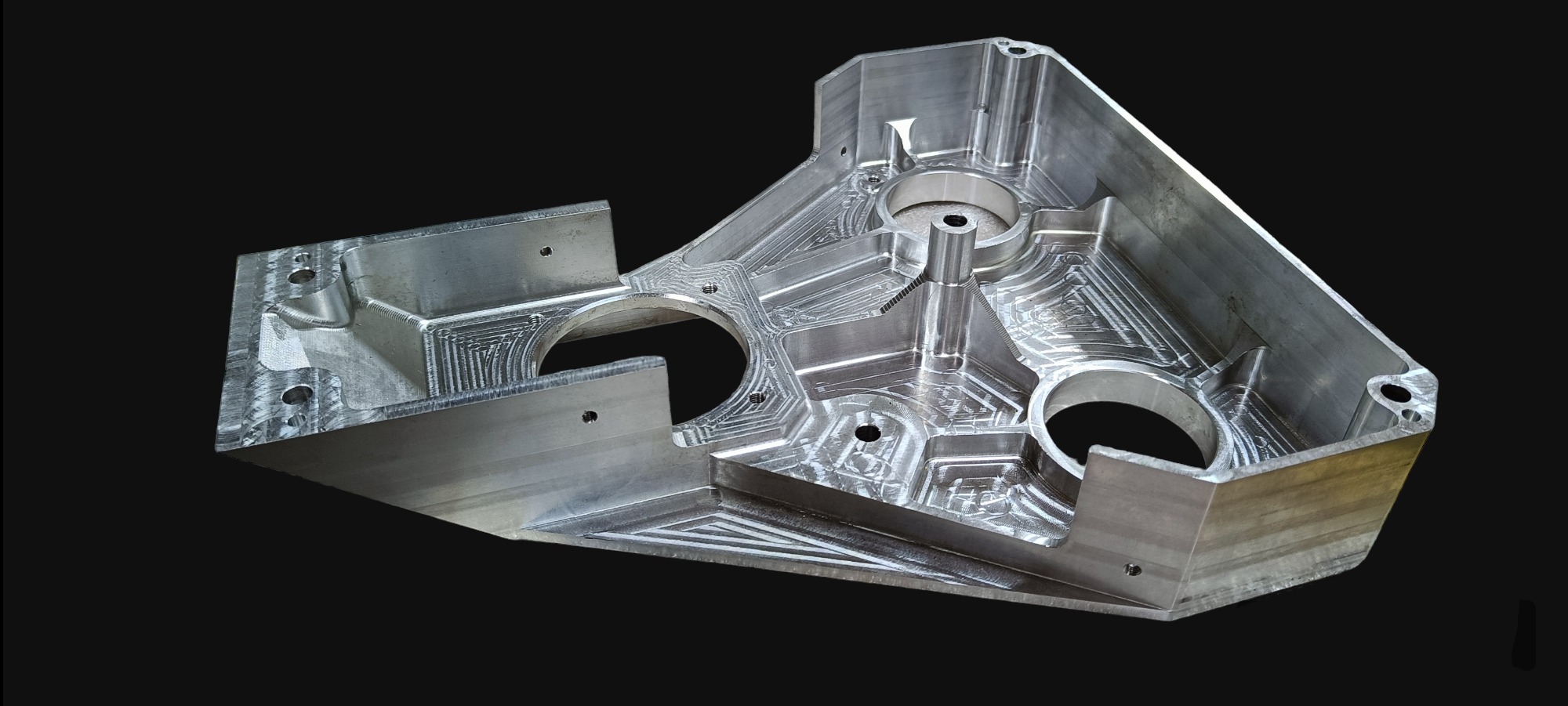 Aluminiowy odlew po obróbce CNC z widocznymi śladami frezowania i otworami montażowymi na czarnym tle.