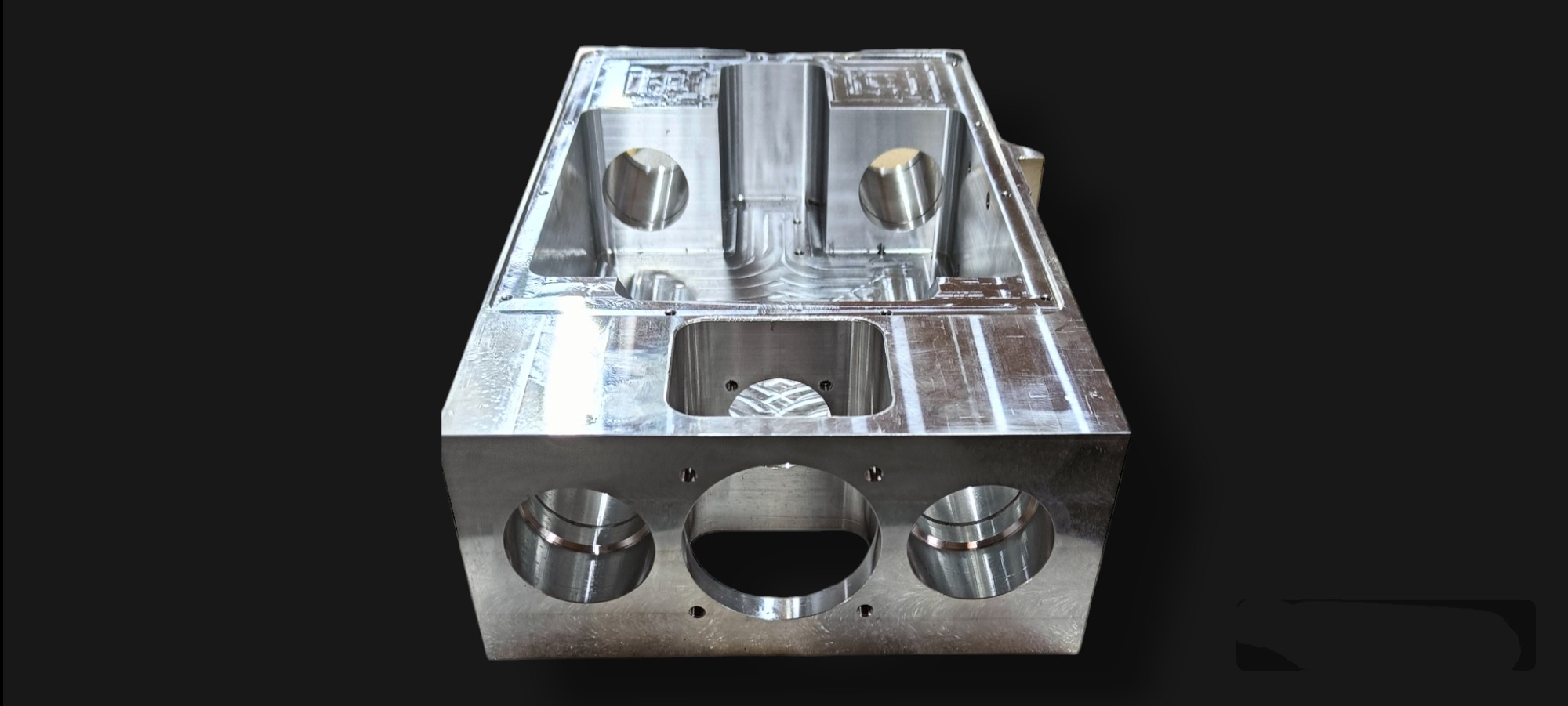 Precyzyjnie wyfrezowany, metalowy blok z licznymi otworami i wgłębieniami, o gładkiej, srebrnej powierzchni, na czarnym tle.