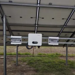 Panel słoneczny z widocznym inwerterem Sofar i skrzynkami elektrycznymi zamontowanymi na konstrukcji wsporczej na zewnątrz budynku.