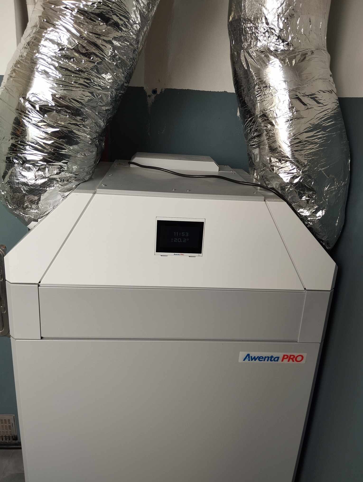 Szara jednostka rekuperacji Awenta PRO z podłączonymi, srebrnymi, elastycznymi przewodami wentylacyjnymi w Poddębicach.