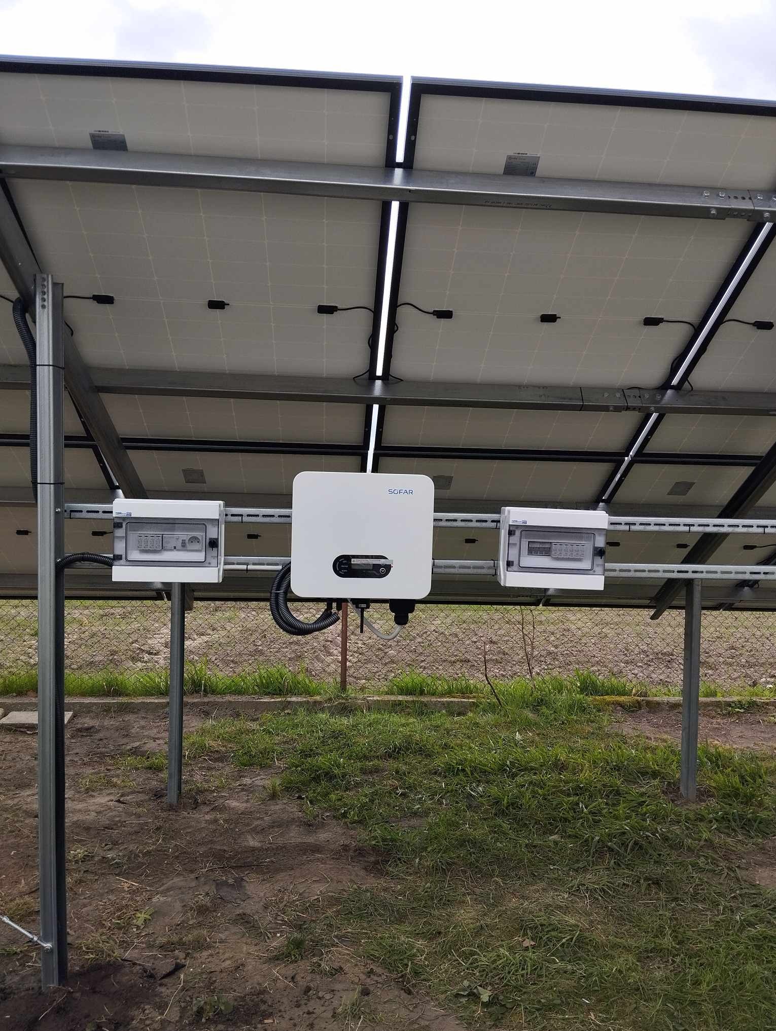 Panel słoneczny z widocznym inwerterem Sofar i skrzynkami elektrycznymi zamontowanymi na konstrukcji wsporczej na zewnątrz budynku.