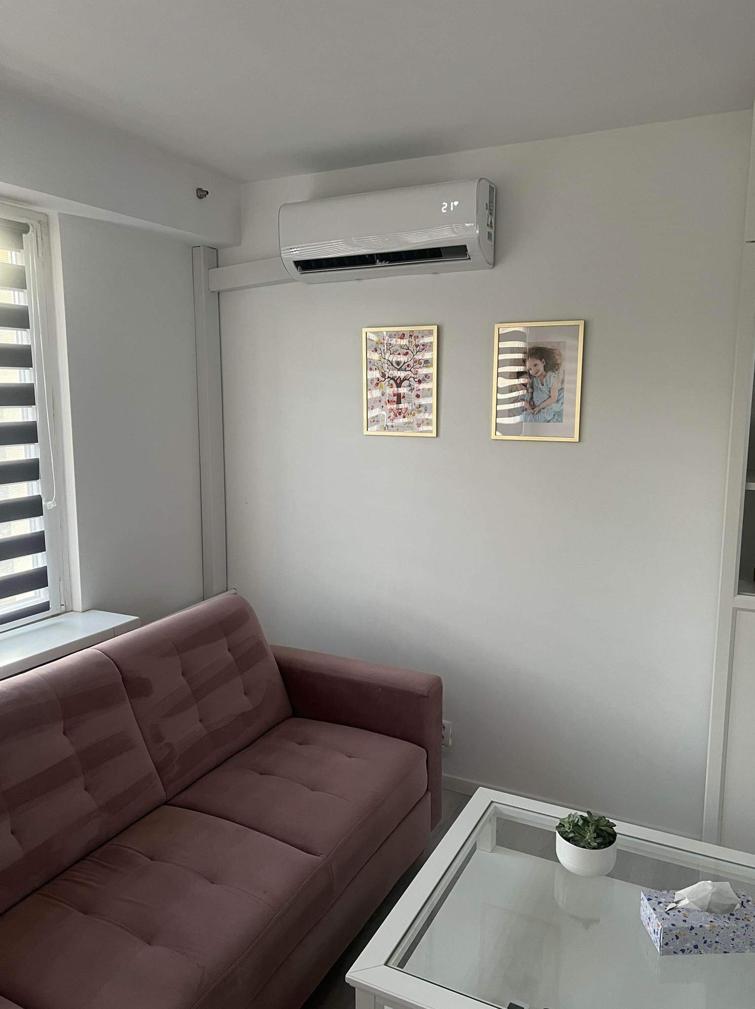 Biała klimatyzacja ścienna z wyświetlaczem temperatury w salonie z różową sofą i stolikiem kawowym.
