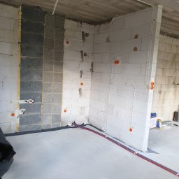 Jakub Zblewski - Surowy stan wnętrza budynku w trakcie prac instalacyjnych: widoczne przewody elektryczne w peszlach na ścianach z betonu komórkowego, rury instalacji wodnej w posadzce, puszki elektryczne. Fragment...
