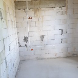 Jakub Zblewski - Surowy stan: Wnętrze w trakcie budowy z widocznymi przewodami elektrycznymi poprowadzonymi po ścianie z betonu komórkowego i niezabezpieczonymi puszkami instalacyjnymi.