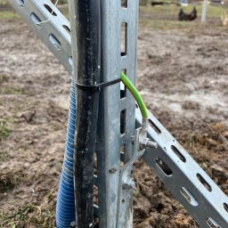 Jakub Zblewski - Uziemienie konstrukcji wsporczej, przewód ochronny żółto-zielony przykręcony do metalowej ramy, obok peszel z kablami, ziemia wokół rozkopana.