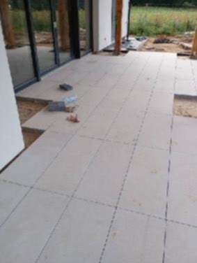 Jasne płyty tarasowe ułożone na podkładzie, widoczne niedokończone fragmenty i przygotowane kostki. Nowoczesny taras w trakcie realizacji.