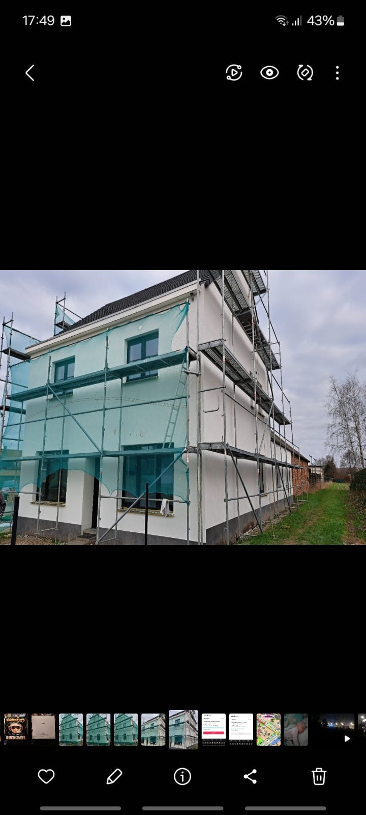 Dom jednorodzinny w trakcie prac elewacyjnych, otoczony rusztowaniami i siatką ochronną. Widoczna świeżo pomalowana, biała elewacja. Ujęcie z dołu, pochmurne niebo w tle.