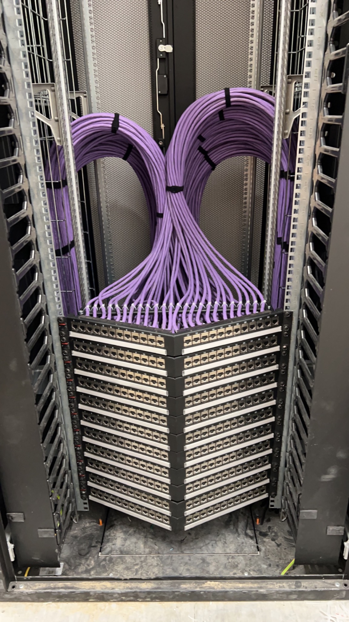 Rząd symetrycznie ułożonych, fioletowych kabli sieciowych, uporządkowanych za pomocą czarnych opasek, podłączonych do panelu krosowniczego w szafie rack.