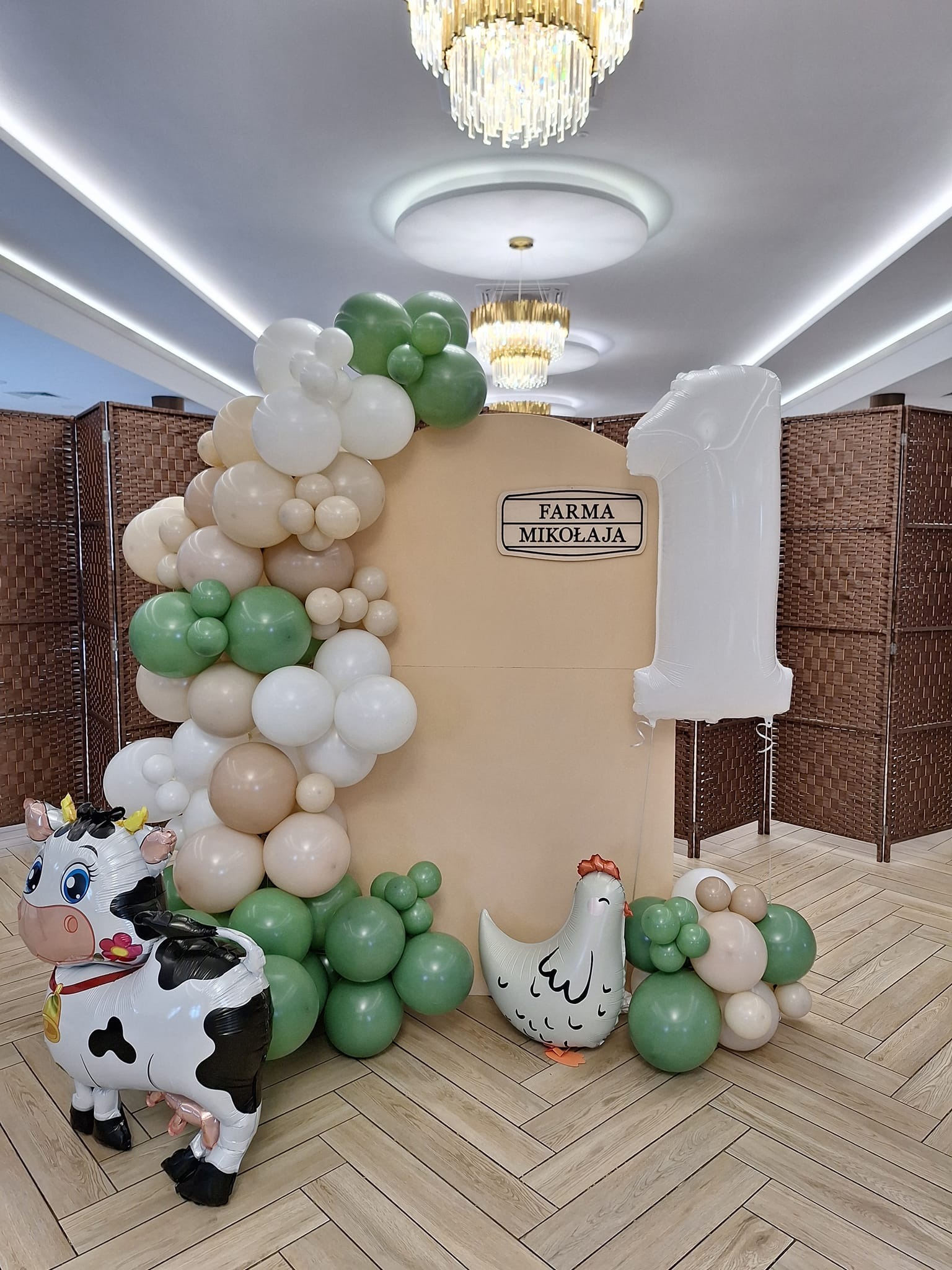 Dekoracja balonowa na pierwsze urodziny z motywem farmy: balon krowa, kurczak i girlanda z zielono-biało-beżowych balonów obok dekoracji z napisem 'Farma Mikołaja' i cyfrą '1'.