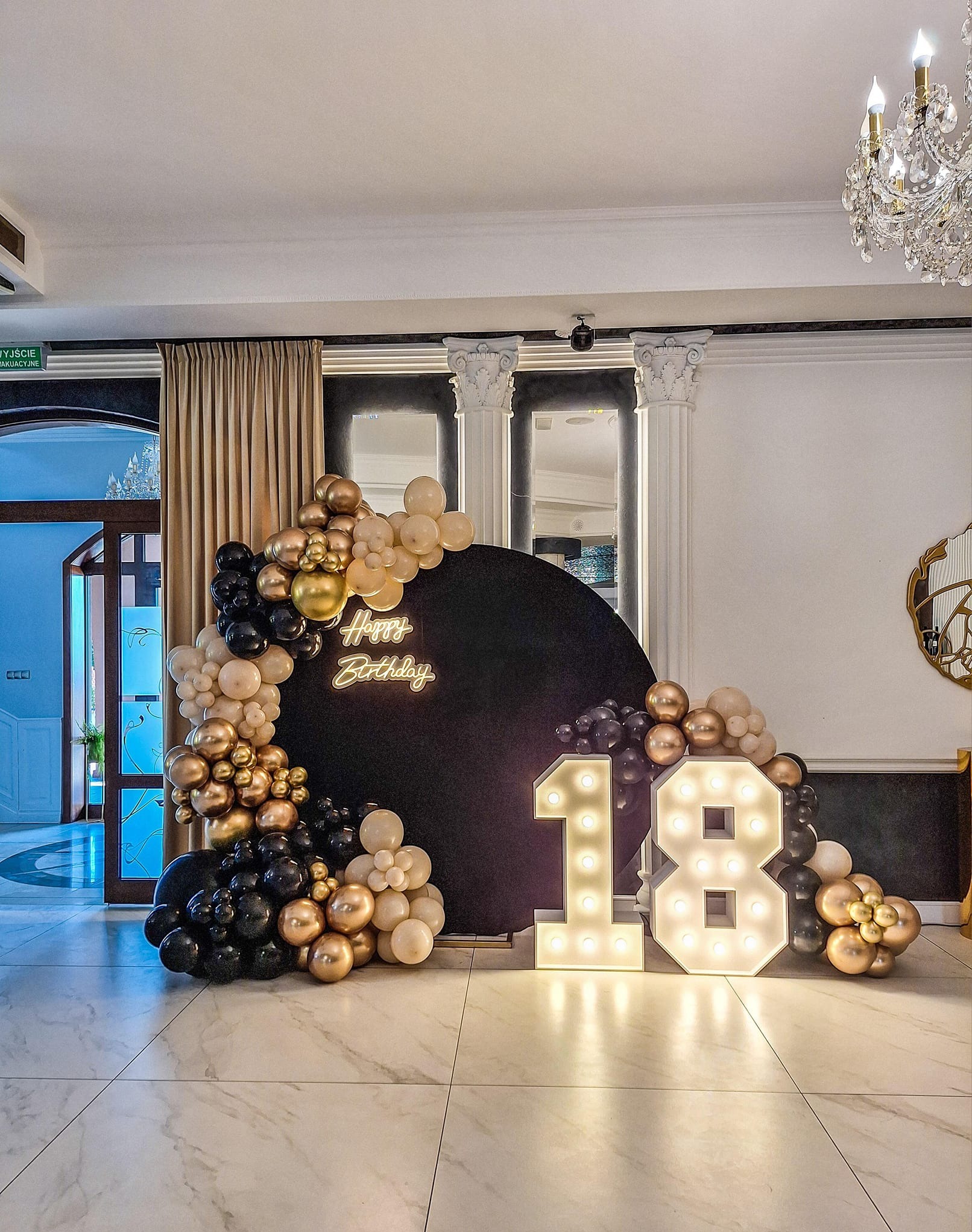 Dekoracja urodzinowa z czarnym tłem, neonowym napisem 'Happy Birthday', girlandą z czarnych, złotych i beżowych balonów oraz podświetlanymi cyframi '18'.
