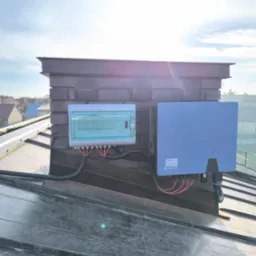 Zamontowana instalacja fotowoltaiczna na dachu, widoczna skrzynka elektryczna i inwerter Solplanet, kable poprowadzone w peszlu. Lekkie zachmurzenie.